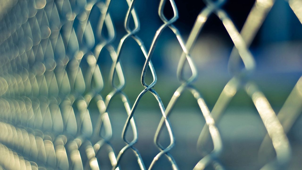 Macro close-up of a chain-link fence with teal and green bokeh — a metaphor for energetic blocks and barriers