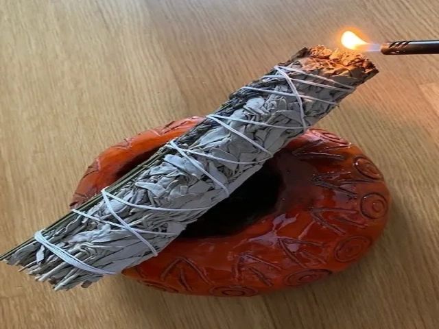 A smudging stick being lit over a decorative red object — used for energetic space clearing